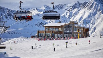 Eine schneebedeckte Berglandschaft mit der Flimjochbahn B2 im Vordergrund. Skifahrer und Snowboarder genießen den Tag auf der Piste.